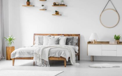 A simplistic college bedroom. There are a couple of plants around the bed and a mirror hanging on the wall.