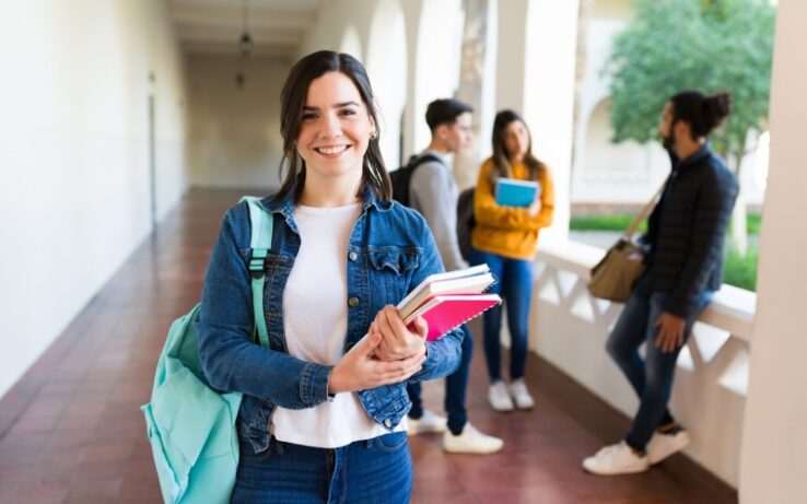 Photo of a young woman wearing a jean jacket and holding her textbooks. She’s heading to her college library to study.