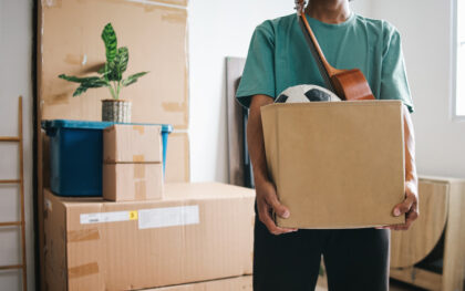 Someone carrying their belongings in boxes into their rental property. The box has a violin and a soccer ball.