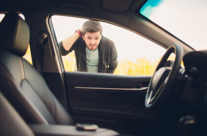 A young man looking exasperated as he stares into his car. His keys are inside, on the center console.