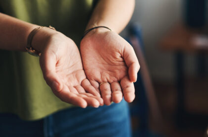 A person in a green shirt holding out their open hands toward the viewer in a gesture of charity and giving.