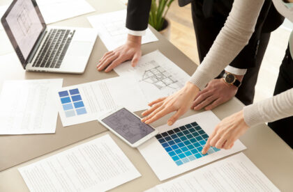 Two interior designers looking at design plans spread across a table. They're deciding on which shade of blue to use.