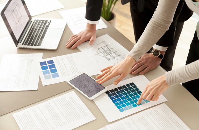 Two interior designers looking at design plans spread across a table. They're deciding on which shade of blue to use.