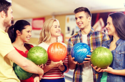 A group of young people standing together in a bowling alley, each holding a different colored bowling ball.
