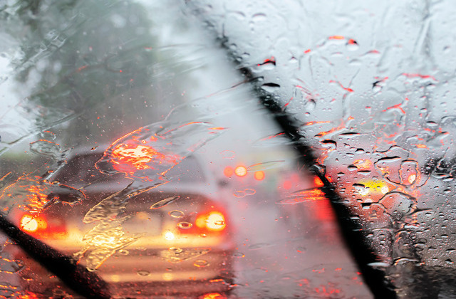 A close-up of a vehicle window while it's raining. The car's windshield wipers are wiping the rain off the front window.