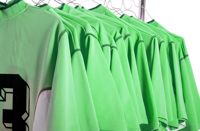A rack full of green soccer jerseys with black numbers on wire hangers stands in front of a white background.
