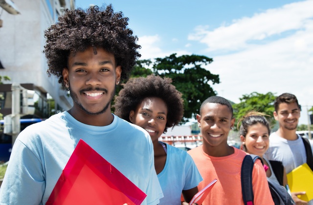 A group of diverse college-aged students standing in line, wearing school accessories, smiling, and dressed casually.