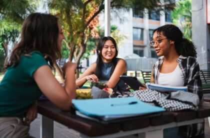 A group of college students working on homework while also eating a healthy snack together at a picnic table.