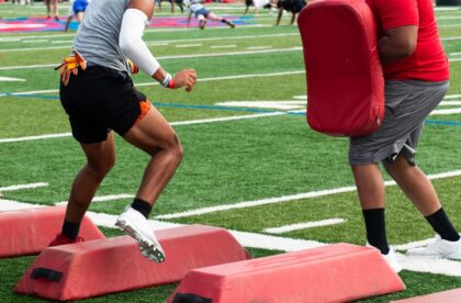 A football player in fitness apparel and cleats side-steps over hurdles during a drill on a turf football field.