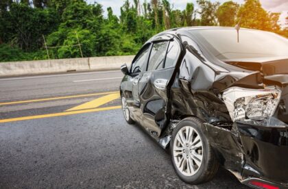 A car is in the middle of the street facing the side of the road. It has heavy damage on the side with large dents.