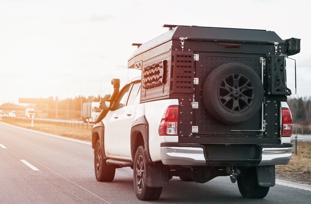 A white pickup truck with a black cargo box and several accessories attached to the back as it drives down the road.