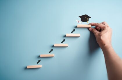 Wooden blocks placed against a blue background in a stair formation with arrows leading up to a graduation cap.
