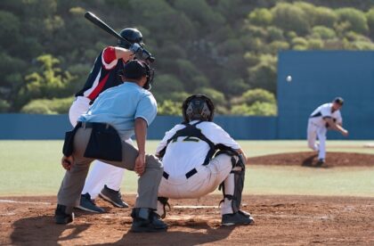 A baseball field with a pitcher throwing to the batter, while the umpire and catcher stand behind the batter.
