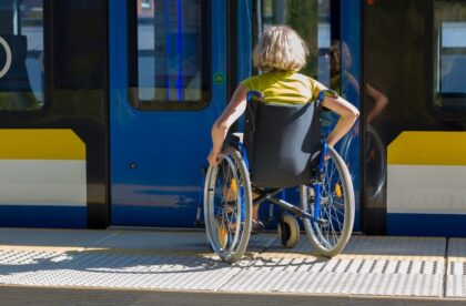 A woman in a wheelchair waiting on a platform for the train doors to open. The train doors are black and blue.