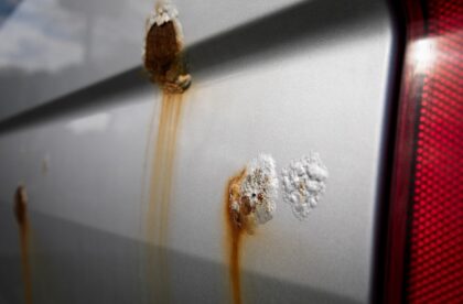 Several rust spots in the surface of a car. The car paint is gray, but the rust spots are a reddish orange color.