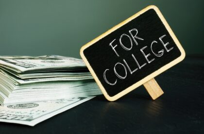 A pile of $100 bills sits on a table with a small chalkboard next to it. It reads the words "For College" in big letters.