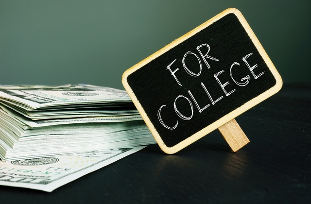 A pile of $100 bills sits on a table with a small chalkboard next to it. It reads the words "For College" in big letters.