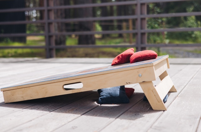 A cornhole board sitting on a deck. There are some bags sitting on top of a board and underneath it.