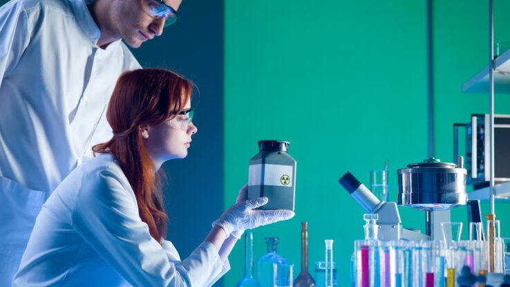 A close-up of two scientists in a lab using chemicals and putting them into a toxic waste container.