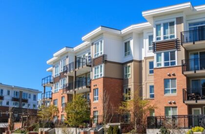 An apartment building with brick at the bottom and beige and white siding. It has balconies with black railings.