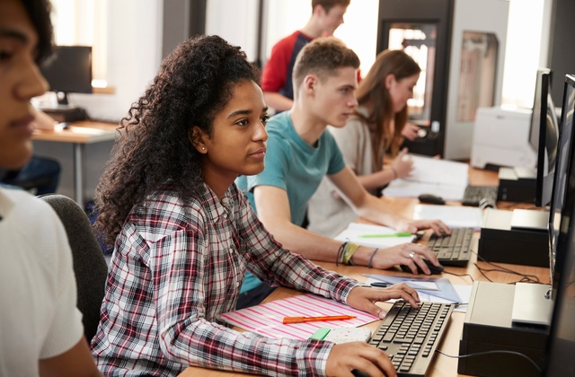 A group of college students sitting at desks in a computer lab while working on design projects independently.