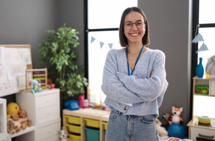A student teacher crosses her arms and smiles while standing in the classroom before the students arrive.