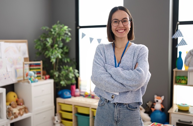 A student teacher crosses her arms and smiles while standing in the classroom before the students arrive.