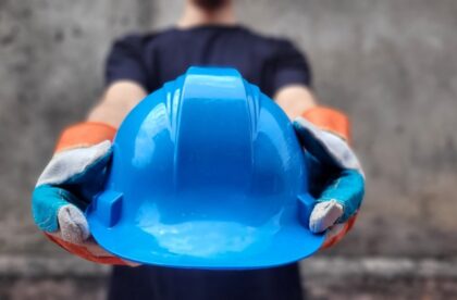 Construction worker offering a blue hard hat, highlighting job site safety, protection, and hands-on trade work.