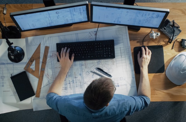An overhead view of an architectural student working on a blueprint, using a desktop computer mouse and keyboard.