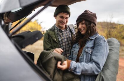 A man and woman pulling sleeping gear out of the back of their vehicle. They both look quite happy.