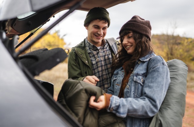 A man and woman pulling sleeping gear out of the back of their vehicle. They both look quite happy.