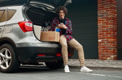 A college student sitting in a car trunk with moving boxes packed around them as they prepare to leave home for college.