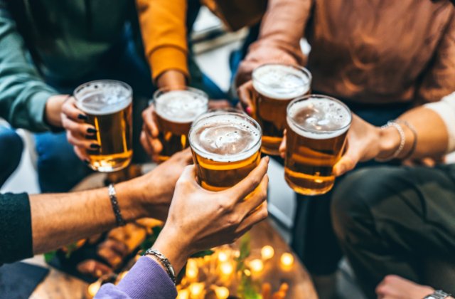 Several people raise glasses of beer together during a casual social gathering, with hands meeting in the center.