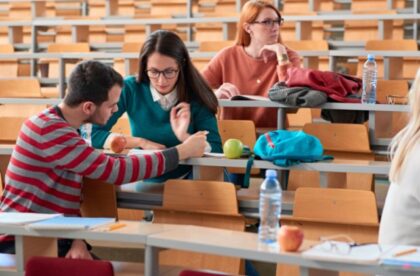 A group of students sitting at lecture hall desks with notebooks, papers, and backpacks while studying together.