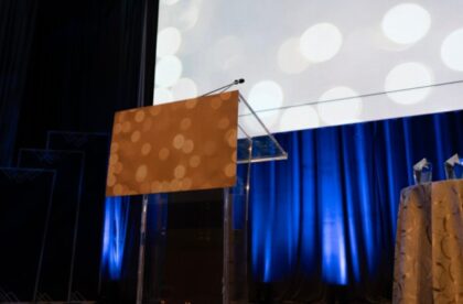 Empty podium with microphones on a blue-lit stage set up for a fundraiser speech.